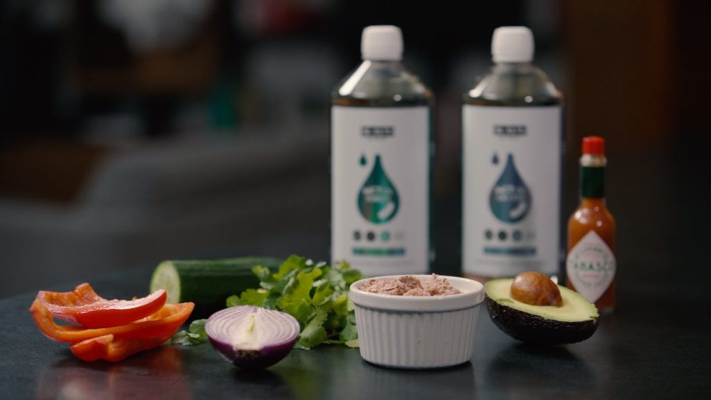 W małej miseczce przygotowany tuńczyk. Po prawej stronie pół awokado. Po lewej czerwona cebula i papryka. W tle pietruszka, ogórek, ostry sos i dwa oleje. Olej MCT C8 i Olej MCT C8+C10