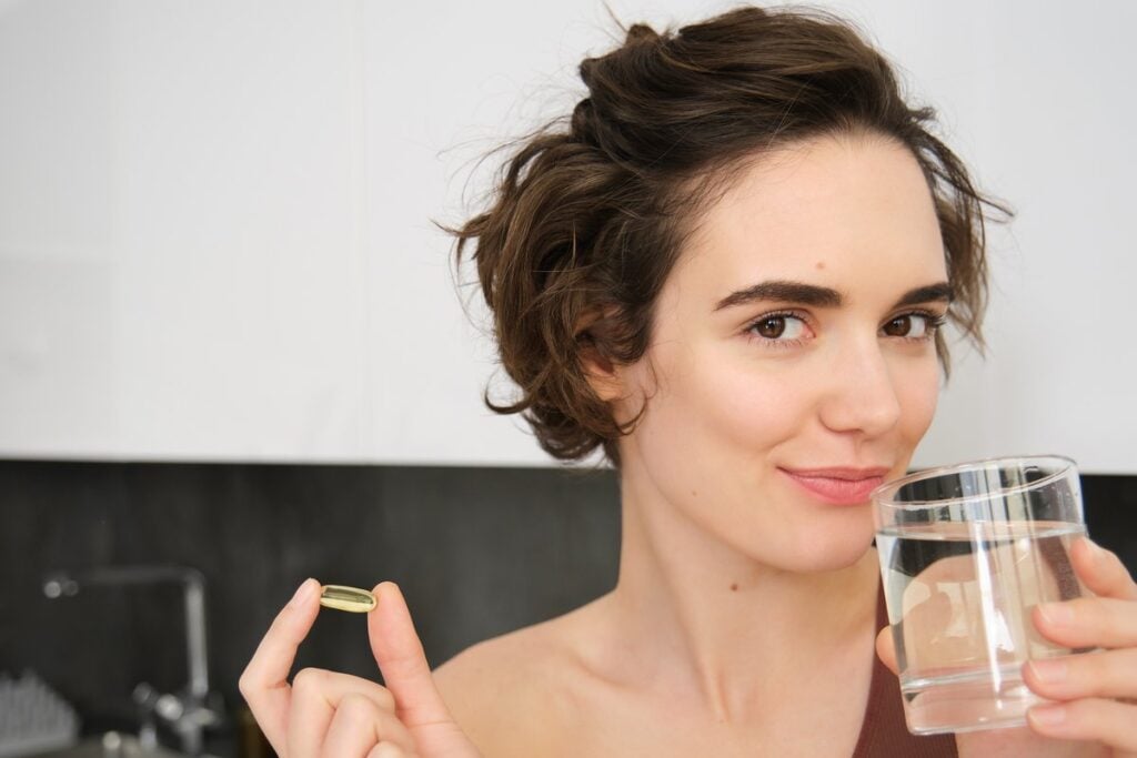 Donna in cucina con una capsula di omega-3 e un bicchiere d'acqua