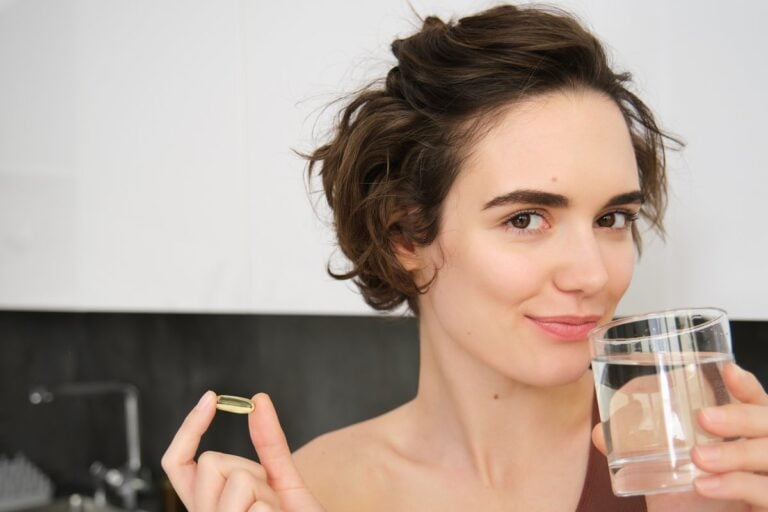 Donna in cucina con una capsula di omega-3 e un bicchiere d'acqua