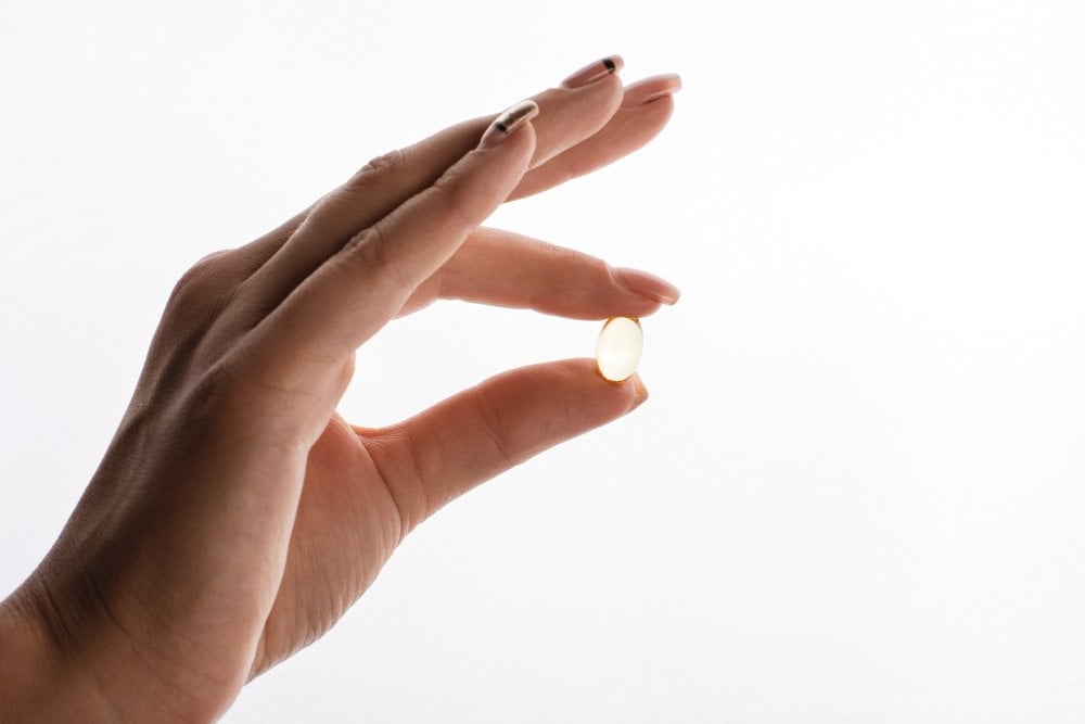 Una mano tiene una capsula di omega-3 tra pollice e indice su sfondo chiaro