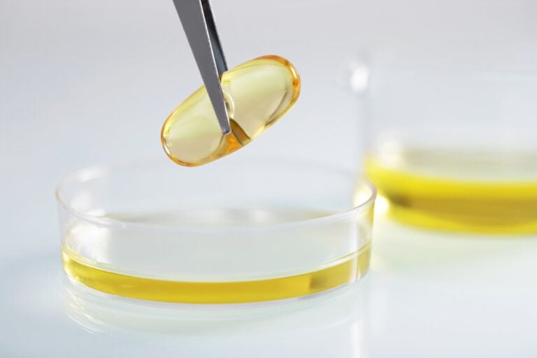 Una pinzetta tiene una capsula gialla sopra una ciotola con olio in laboratorio