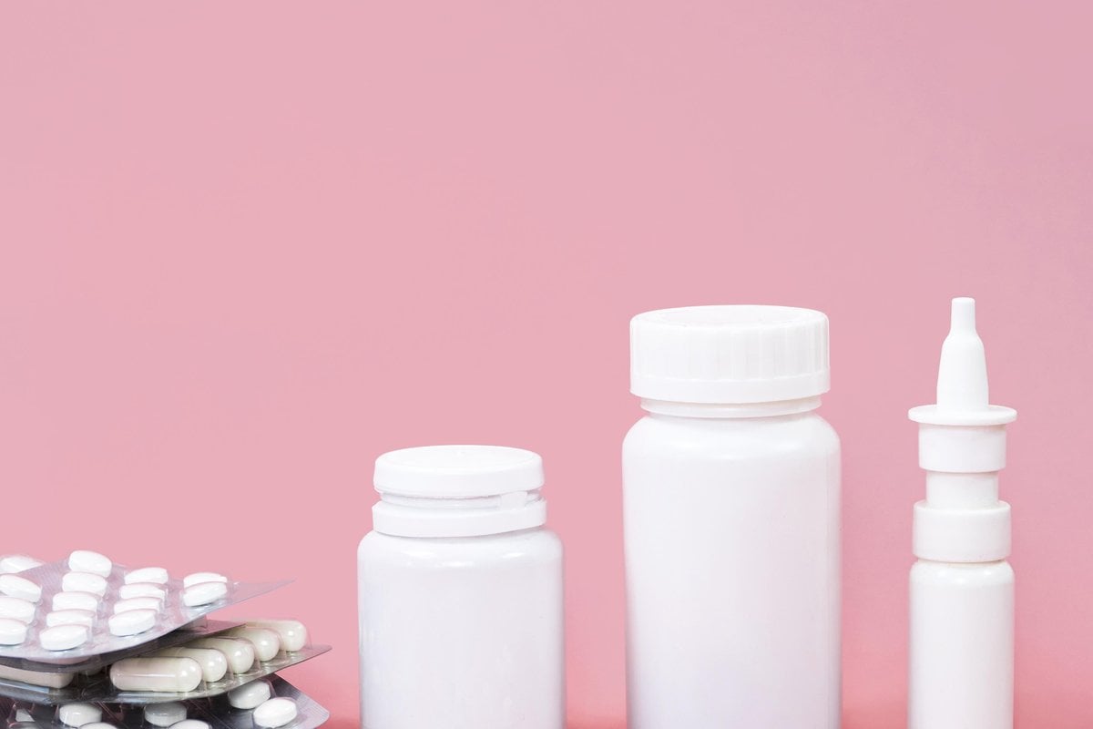 Flaconi bianchi per compresse, blister e capsule sparse su sfondo rosa